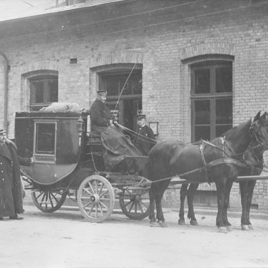 Sort-hvid foto: Postvognen / diligencen foran Jyderup Station. På bukken sidder Niels Jensen, i pels ved siden af står postkonduktør Jespersen og bag vognen postfuldmægtig Lynge. Datering: ca. 1905.