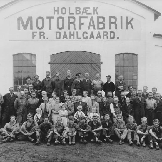 Sort-hvid foto af en gruppe mennesker opstillet foran porten til Holbæk Motorfabrik.