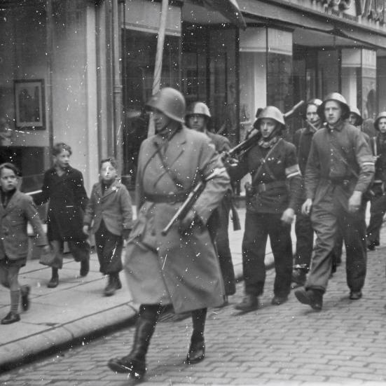 Sort-hvid foto af en gruppe modstandsfolk marcherende i række med børn på fortovet, der ser til.