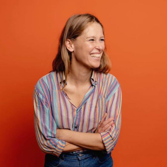 Portræt af en grinende Lea Korsgaard på orange baggrund.