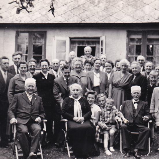 Sort-hvid foto af en stor flok mennesker opstillet til foto udendørs.