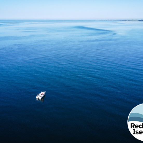 Blåt hav set fra luften med båd, der sejler mod horisonten. Foreningen Red Isefjords logo i højre hjørne.