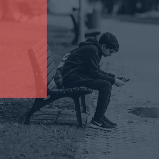 Foto af ensom dreng på en bænk med sin telefon