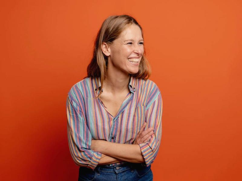 Portræt af en grinende Lea Korsgaard på orange baggrund.