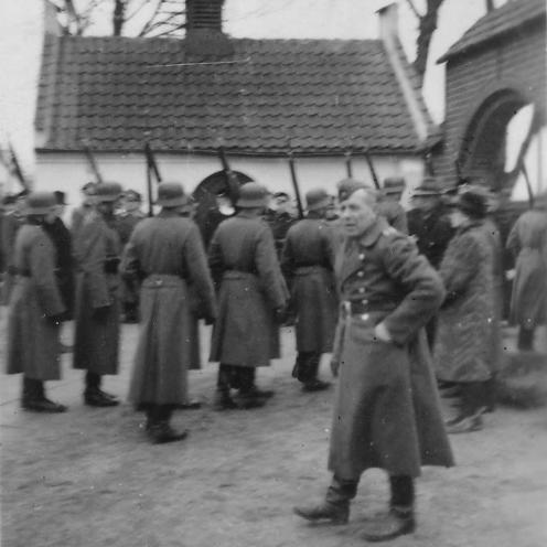 Sort-hvid foto: Tysk æreskompagni ved begravelsen for de allierede flyvere i Tveje Merløse Kirke. Mænd i uniformer på geled med gevær. En mand vender ansigtet mod kameraet.