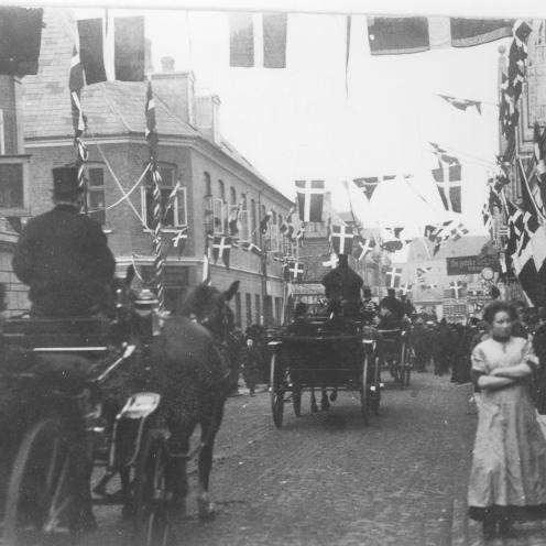 Sort-hvid foto: “Fine folk”, heriblandt kong Frederik d. 8 og dronning Louise, kører igennem Nygade i forbindelse med indvielsen af byens nye rådhus den 11. februar 1911.