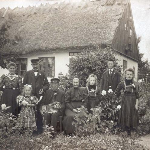 Sort-hvid foto: Familie opstillet uden for et stråtækt hus.