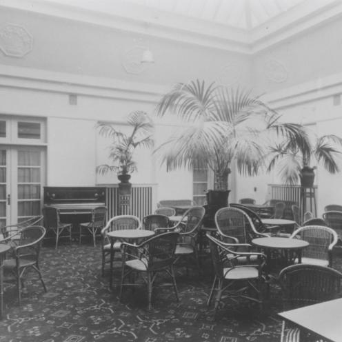 Sort-hvid foto af stue med runde borde, polstrede stole og palmer.