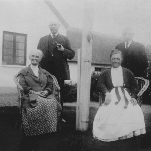 Sort-hvid foto af to ældre par. Kvinderne sidder i kurvestole ved siden af hinanden, mændene står bag deres koner.