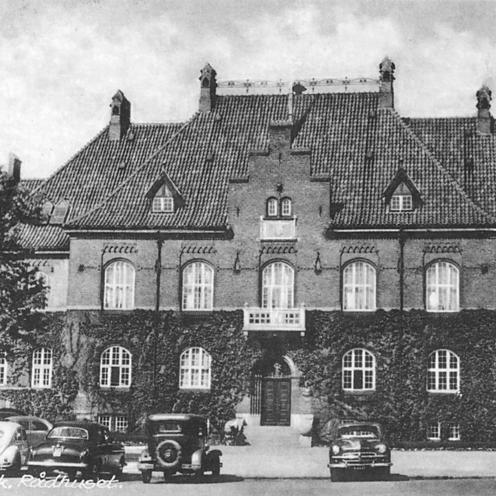 Sort-hvid foto af Holbæk tidligere rådhus med gammeldags biler parkeret foran.