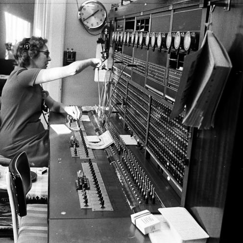 Kvindelig medarbejder betjener en manuel telefoncentral med stikforbindelser og headset.