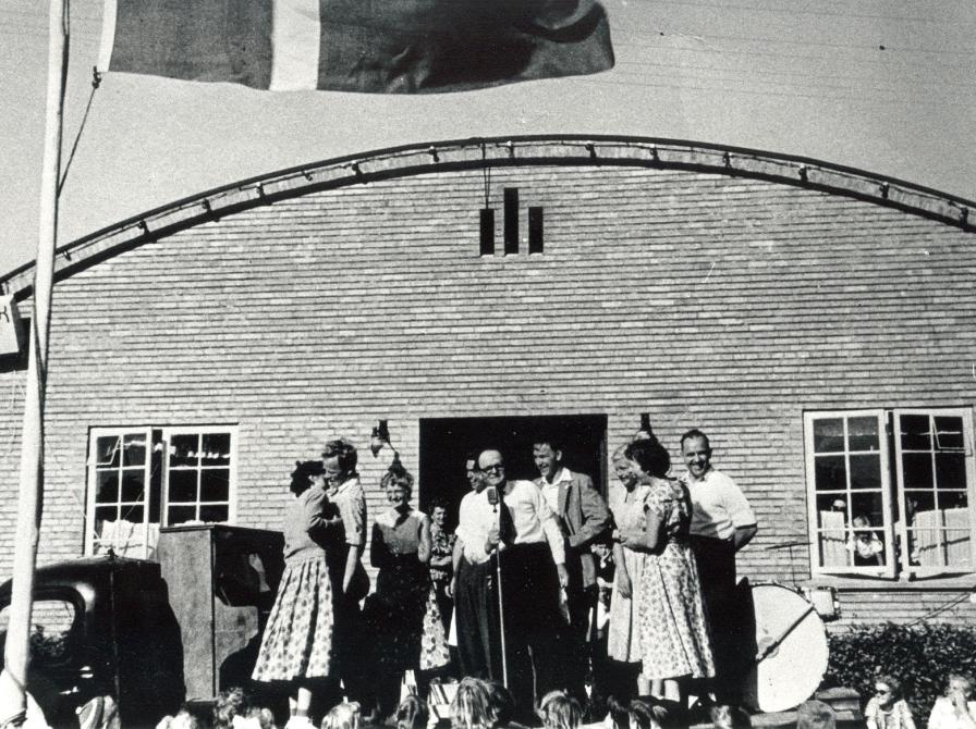 Sort-hvid foto: Udendørs optræden af Gøglervognen ved forsamlingshuset i Stigs Bjergby. Dannebrog er hejst i flagstangen.