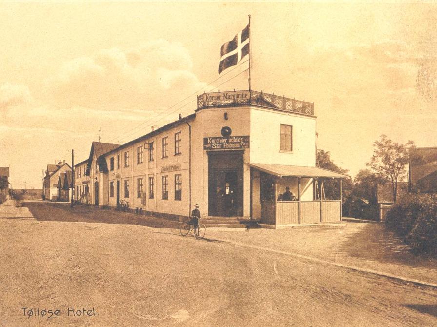 Sort-hvid foto: Tølløse Hotel med tagterrasse, flag - og reklame for Korsør Margarine. Set fra gaden.