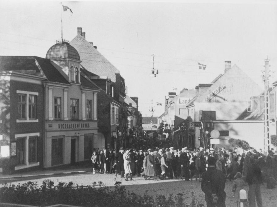 Sort-hvid foto: En folkemængde bevæger sig forbi Nicolaisens Hotel på hjørnet af Nygade.