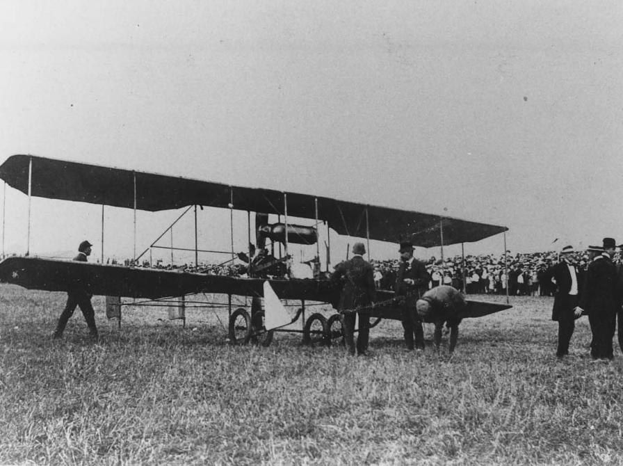 Sort-hvid foto af folk foran en dobbeltdækkerflyver.