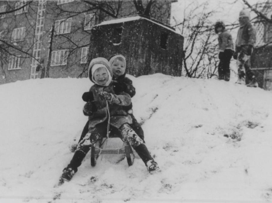 Sort-hvid foto af to børn på en kælk på vej ned ad bakke.