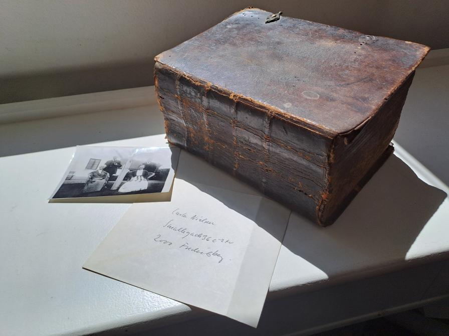 Farvefoto af en tyk skindindbundet bog samt et foto og en konvolut.