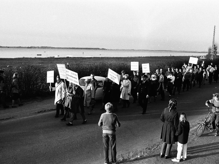 Sort-hvid foto af demonstrationstog med skilte uden for byen.