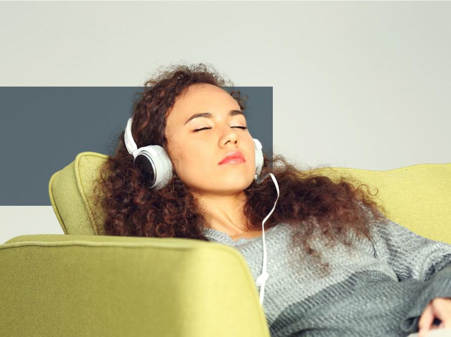 Kvinde sidder lænet tilbage i en sofa med lukkede øjne med hovedtelefoner på