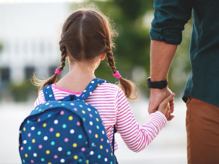 Pige går med skoletaske og sin far i hånden